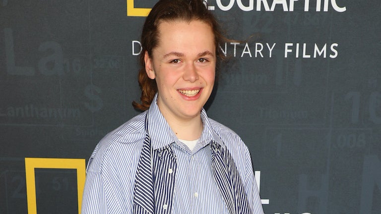Robbie Barrat smiling in a striped shirt in front of a step and repeat backdrop